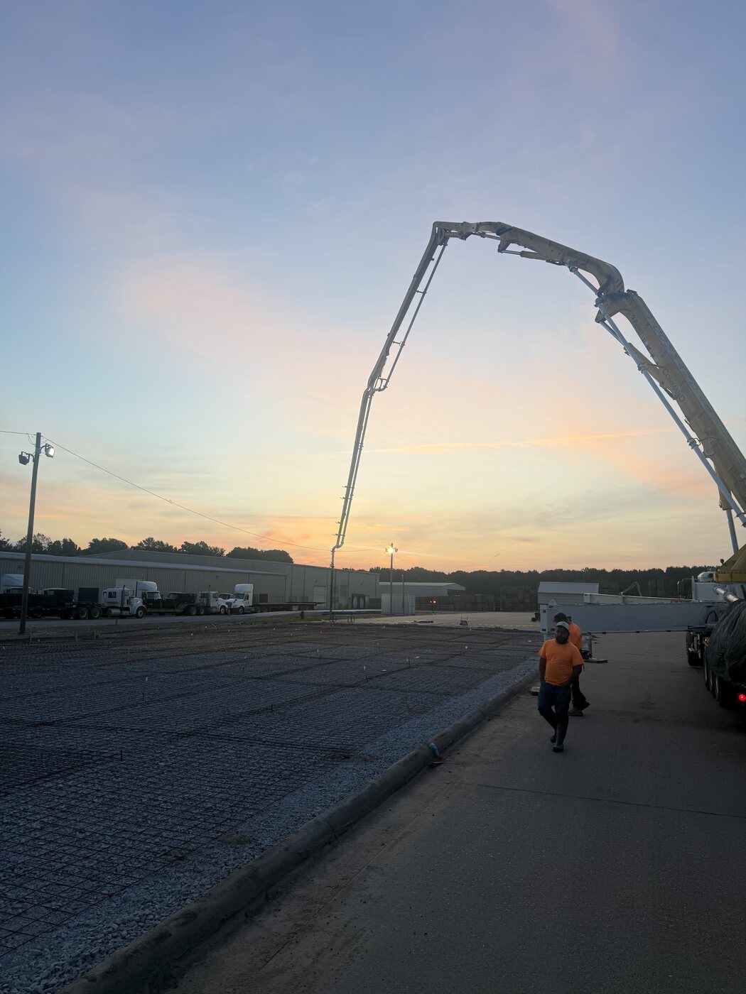 Concrete pump boom at sunrise placing concrete pavement over rebar along a commercial site drive